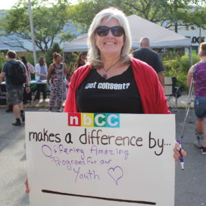 Woman holds a sign that reads nbCC makes a difference by offering amazing programs for youth